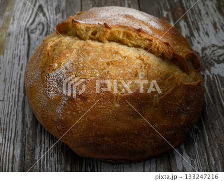 Freshly baked crusty bread resting on rustic wooden table inviting warmth and comfort Freshly baked crusty bread resting on rustic wooden table inviting warmth and comfort 133247216