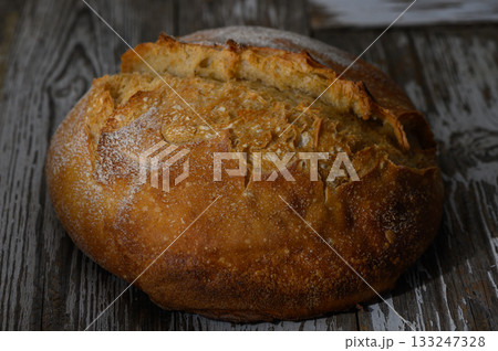 Freshly baked artisan bread resting on rustic wooden table under warm light Freshly baked artisan bread resting on rustic wooden table under warm light 133247328