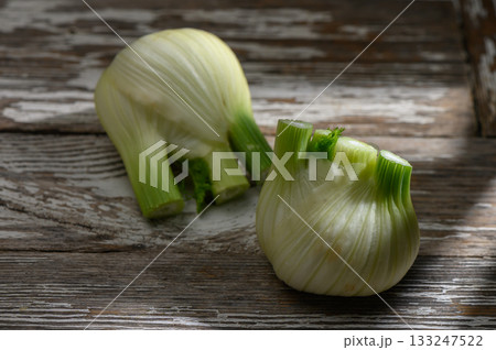 Freshly cut fennel bulbs resting on rustic wooden surface bathed in warm light 133247522
