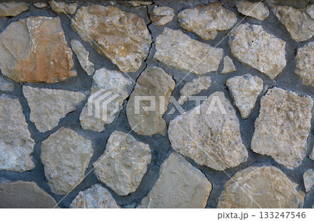 Textured stone wall showcasing natural patterns and earthy tones in sunlight 133247546