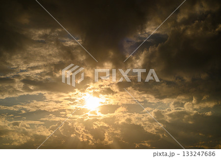 Golden rays pierce through dramatic clouds during a tranquil sunset sky 133247686