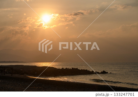 Golden sunset casts warm hues over tranquil shoreline and gentle waves near distant hills Golden sunset casts warm hues over tranquil shoreline and gentle waves near distant hills 133247701