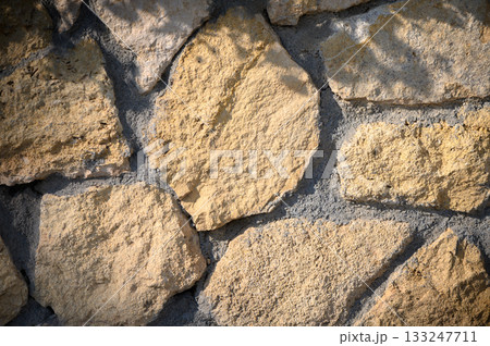Rustic stone wall showcasing intricate textures and natural patterns under sunlight in a tranquil setting Rustic stone wall showcasing intricate textures and natural patterns under sunlight in a tranquil setting 133247711