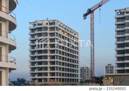 Urban development project with modern buildings rising under construction crane at twilight 133248083