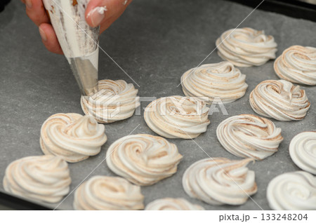 Delicate swirls of meringue being piped onto a baking tray in a cozy kitchen during afternoon baking 133248204