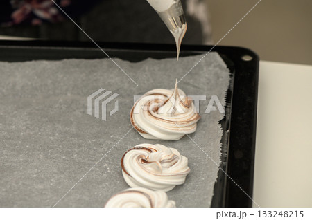 Delicate swirls of meringue being piped onto a baking tray during a sweet culinary endeavor Delicate swirls of meringue being piped onto a baking tray during a sweet culinary endeavor 133248215