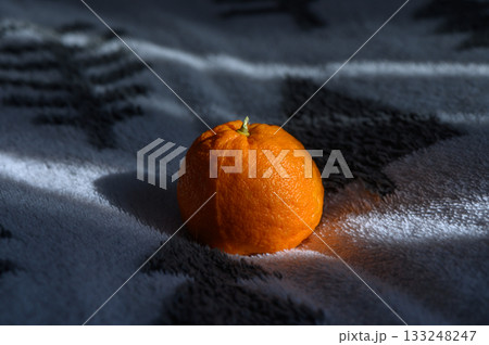 Bright orange mandarin resting on a cozy blanket in soft morning light Bright orange mandarin resting on a cozy blanket in soft morning light 133248247