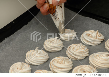 Creative pastry chef piping elegant meringue swirls on parchment for delightful desserts Creative pastry chef piping elegant meringue swirls on parchment for delightful desserts 133248367