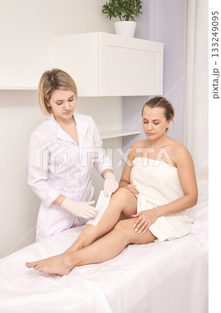 Young caucasian female receiving leg waxing treatment in spa by professional Young caucasian female receiving leg waxing treatment in spa by professional 133249095
