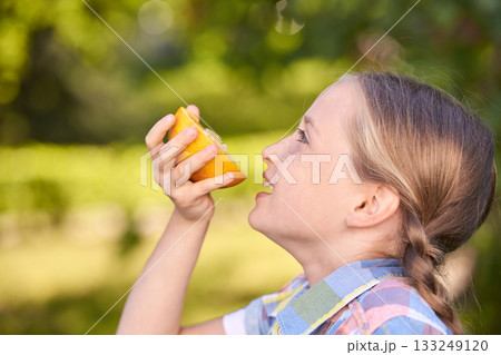 Caucasian young girl enjoying a fresh orange slice in sunny orchard setting Caucasian young girl enjoying a fresh orange slice in sunny orchard setting 133249120