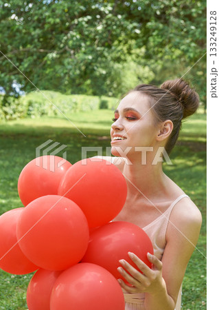 Young caucasian female holding red balloons in sunny park with joyful Young caucasian female holding red balloons in sunny park with joyful 133249128