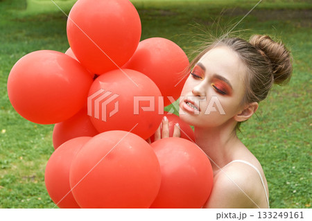 Young caucasian female with bright makeup holding red balloons outdoors Young caucasian female with bright makeup holding red balloons outdoors 133249161