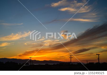 Dramatic sunset paints the sky with vibrant hues over tranquil hills and power lines in the evening light Dramatic sunset paints the sky with vibrant hues over tranquil hills and power lines in the evening light 133249325