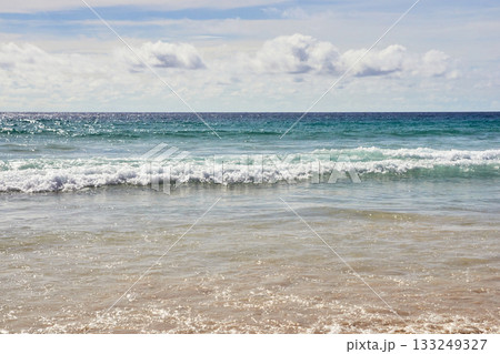 Tranquil ocean waves meeting sandy shore under clear sky on peaceful beach day Tranquil ocean waves meeting sandy shore under clear sky on peaceful beach day 133249327