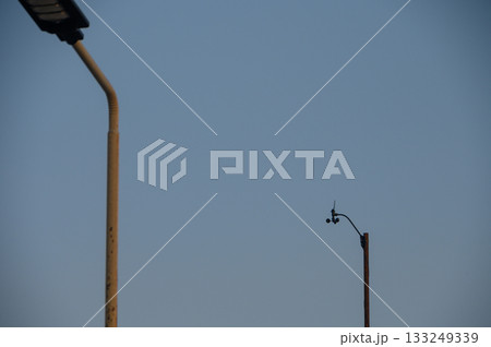Urban landscape featuring streetlights and surveillance camera against a clear sky at dusk Urban landscape featuring streetlights and surveillance camera against a clear sky at dusk 133249339