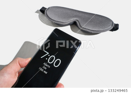 Smartphone alarm displayed at 7 am with gray sleep mask on white surface 133249465