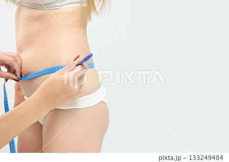 Young caucasian female measuring waist with tape for fitness tracking and health Young caucasian female measuring waist with tape for fitness tracking and health 133249484