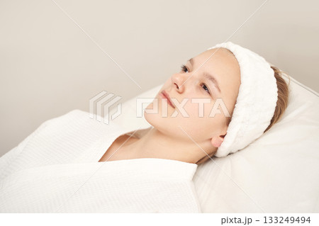 Young caucasian female relaxing in spa wearing headband and white robe 133249494