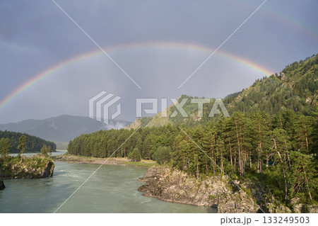 Majestic double rainbow over forested mountains and river under cloudy sky 133249503
