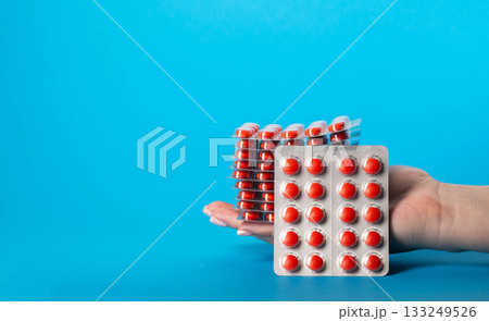 Stack of red pills in hand on blue background for edema. Diuretic pills for urethritis. Copy space for text, metabolism 133249526