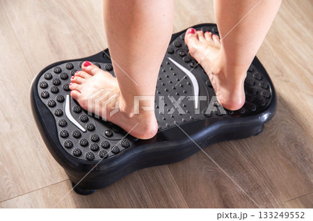 Women's legs stand on a sports vibration platform at home. Concept of doing sports at home. Modern home exercise machine, close-up Women's legs stand on a sports vibration platform at home. Concept of doing sports at home. Modern home exercise machine, close-up 133249552