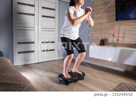 Brunette girl doing sports at home on a modern sports vibration platform. Concept of cellulite elimination and weight loss, background 133249558