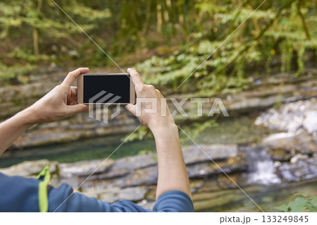 Caucasian male taking photo of scenic forest stream with smartphone in nature 133249845