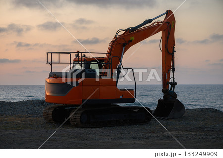 Excavator poised for work at the shoreline during a tranquil sunset over the ocean Excavator poised for work at the shoreline during a tranquil sunset over the ocean 133249909