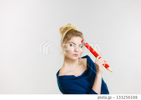 Woman holding big oversized pencil thinking about something 133250108