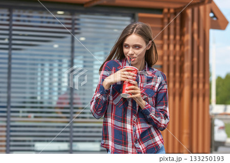 Young caucasian female enjoying a soda outdoors in casual plaid shirt 133250193