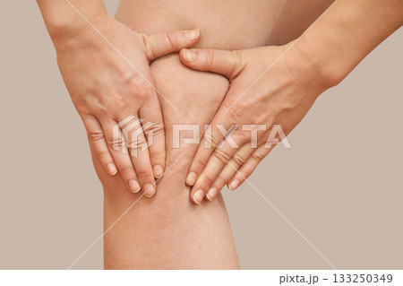 Female caucasian adult examining knee with hands on neutral background 133250349