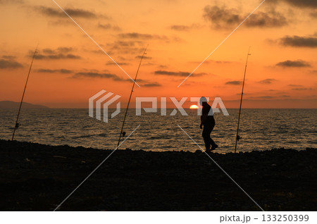 Sunset fishing by the ocean with tranquil waves and shadows dancing on the shore Sunset fishing by the ocean with tranquil waves and shadows dancing on the shore 133250399