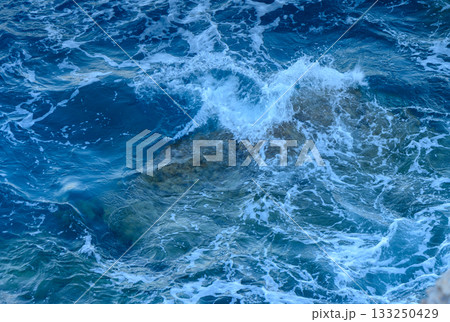 Waves crashing over sunlit rocks in the turquoise waters of a serene coastal destination. 133250429