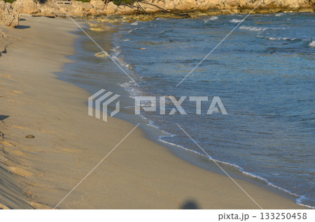 Tranquil shoreline at sunset with gentle waves lapping against golden sand and rocky cliffs. Tranquil shoreline at sunset with gentle waves lapping against golden sand and rocky cliffs. 133250458