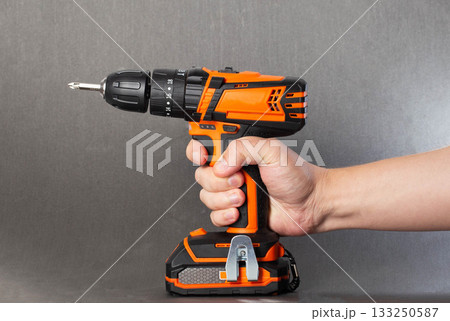 Hand holding a cordless drill against a gray background for home improvement and DIY tasks 133250587