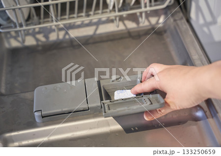 Hand placing dishwasher tablet in open dishwasher tray 133250659