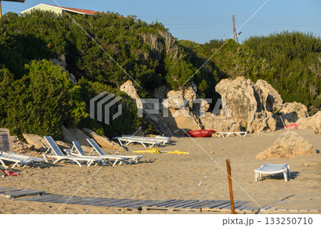 Relaxing beachside view with loungers and rocky cliffs at sunset on a serene coastal afternoon. 133250710