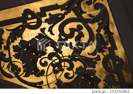 Intricate black iron scrollwork silhouetted against a rich gold background, 133250862