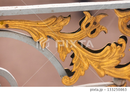 Close-up of gilded gold leaf scrollwork on a decorative metal balustrade Close-up of gilded gold leaf scrollwork on a decorative metal balustrade 133250863