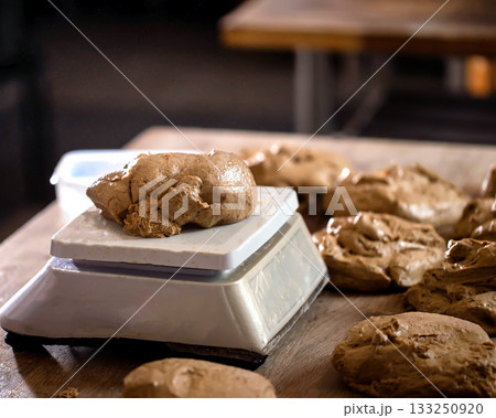 Dough portion placed on digital scale for precise measurement during food preparation process in bakery kitchen. Multiple dough pieces ready for baking. 133250920