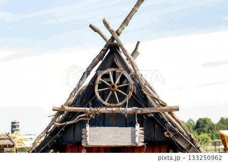 Wooden roof of an old village hut with an old horse-drawn carriage wheel and a sign for an inscription Wooden roof of an old village hut with an old horse-drawn carriage wheel and a sign for an inscription 133250962