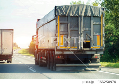 A truck pulls a grain semi-trailer with grain against the backdrop of the sun on a highway, industry A truck pulls a grain semi-trailer with grain against the backdrop of the sun on a highway, industry 133250970