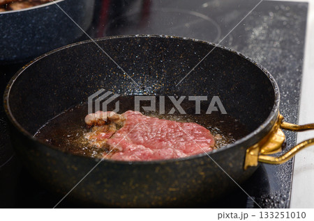 Sizzling steak cooking in a frying pan on a modern stovetop in a cozy kitchen setting Sizzling steak cooking in a frying pan on a modern stovetop in a cozy kitchen setting 133251010