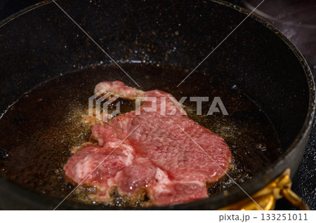 Cooking a juicy steak in hot oil in a skillet on the stove during a cozy evening at home Cooking a juicy steak in hot oil in a skillet on the stove during a cozy evening at home 133251011