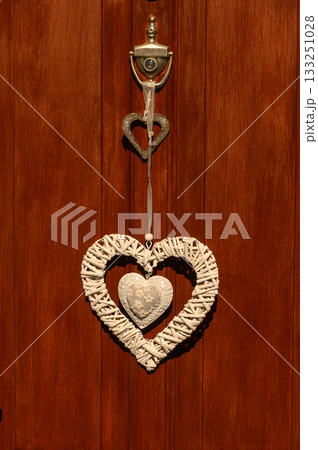 Rustic heart-shaped door ornament hanging against a warm wooden background in bright sunlight 133251028