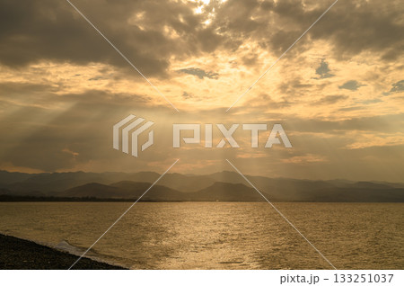 Golden rays shine through clouds over tranquil waters at sunset in a picturesque landscape 133251037