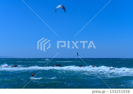 Kite surfer leaps over waves under a bright blue sky at the beach during a sunny afternoon Kite surfer leaps over waves under a bright blue sky at the beach during a sunny afternoon 133251038