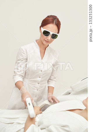 Female practitioner performing laser hair removal on client in clinical setting 133251300