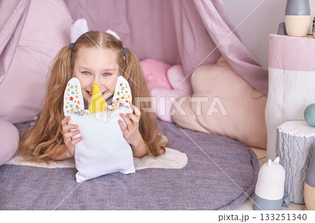 Smiling caucasian young girl in playful bedroom holding stuffed unicorn pillow Smiling caucasian young girl in playful bedroom holding stuffed unicorn pillow 133251340