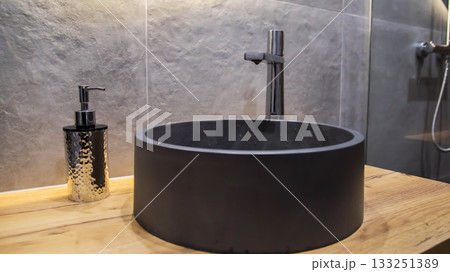 Stylish modern gray stone sink in the bathroom in a suspended wooden cabinet and a chrome tap. Gray tiles on the wall, interior 133251389